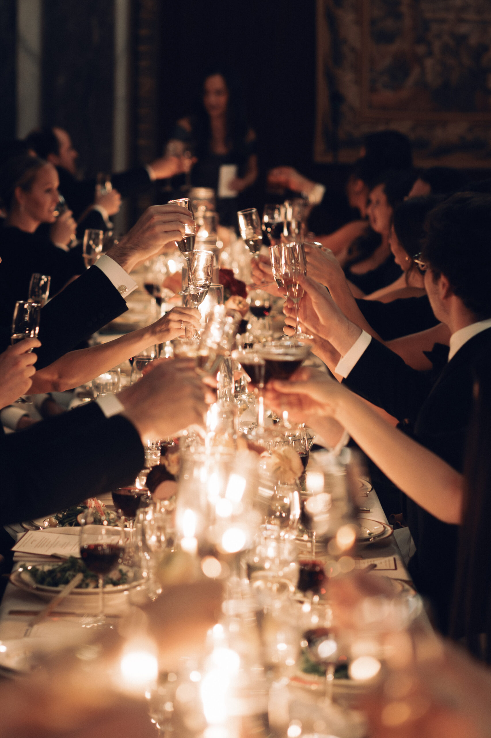 Guests seated at long tables in dim, romantic lighting, clinking glasses 