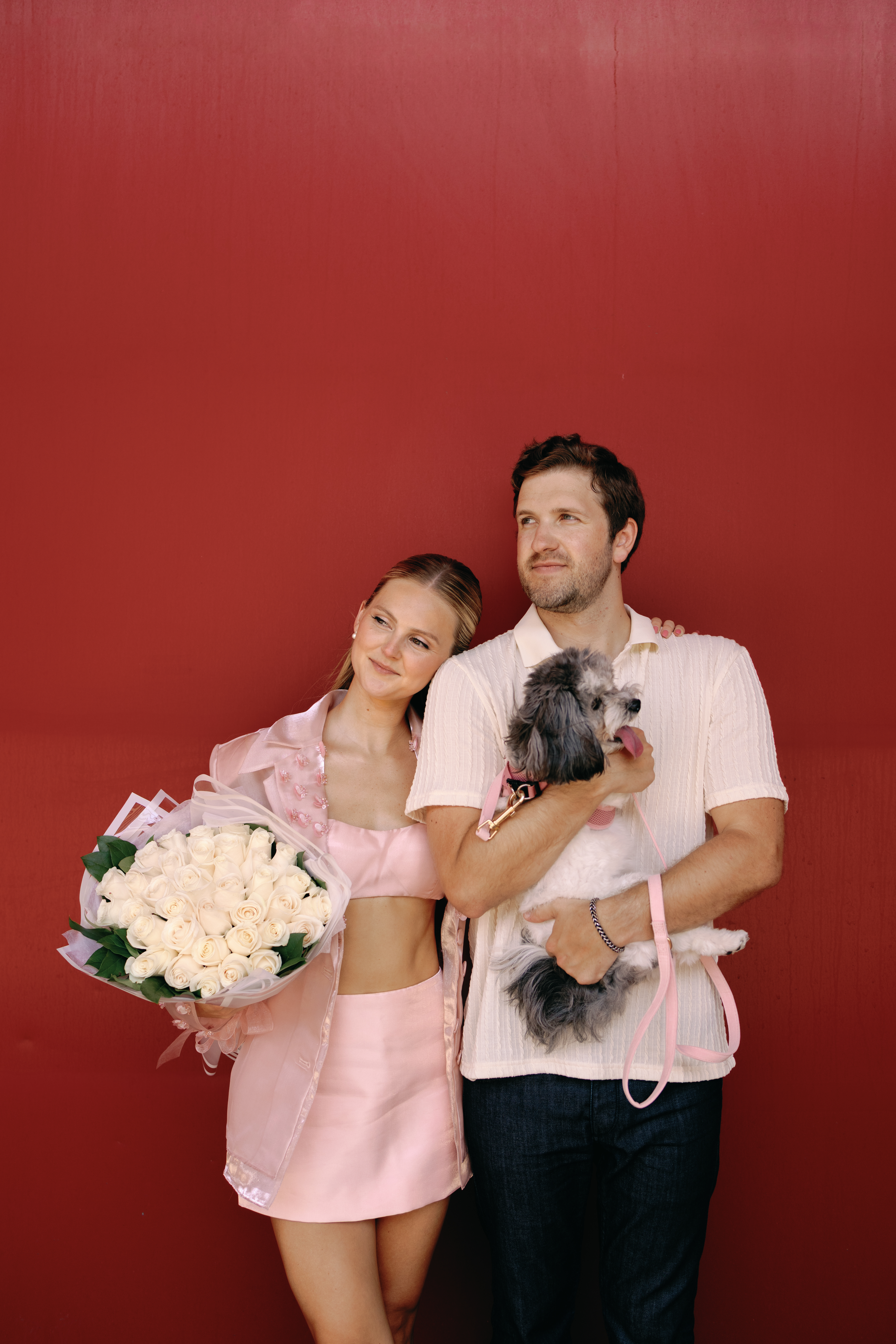 Couple walking through Manhattan streets in candid engagement moment with flowers and dog